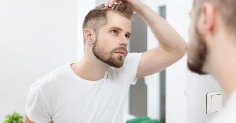 young bearded man looking in mirror at hair after covid hair loss